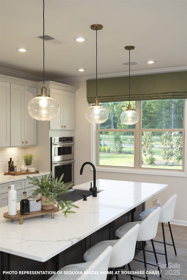 kitchen with a kitchen breakfast bar, stainless steel double oven, visible vents, and crown molding