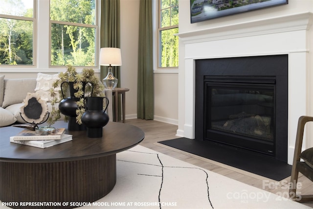 living room with a glass covered fireplace, plenty of natural light, baseboards, and wood finished floors