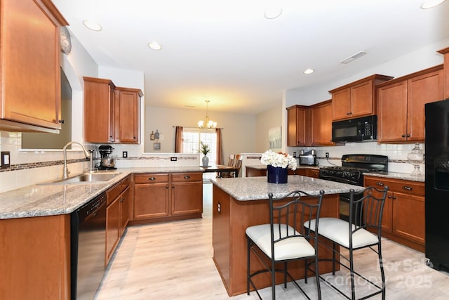 kitchen with a notable chandelier, black appliances, sink, decorative light fixtures, and kitchen peninsula