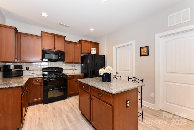 kitchen with decorative backsplash, light stone counters, black appliances, a center island, and light hardwood / wood-style floors