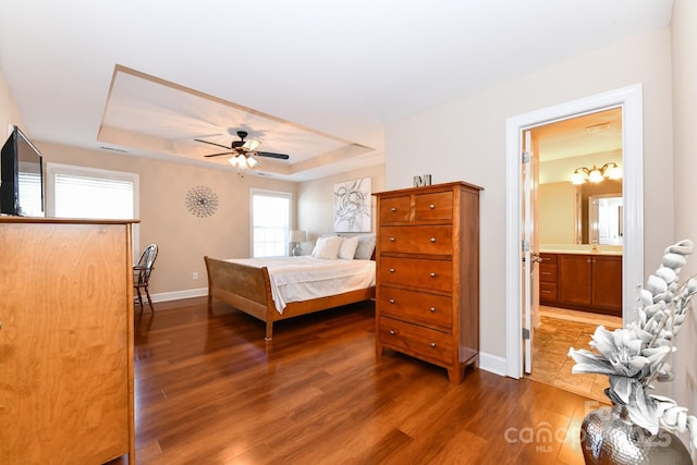 bedroom featuring a raised ceiling, ceiling fan, dark wood-type flooring, and ensuite bathroom