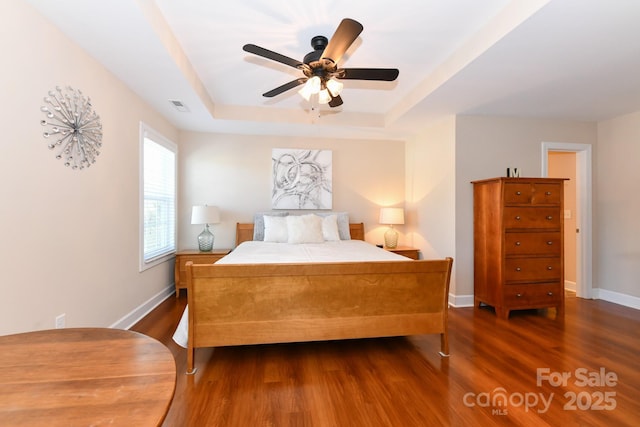 bedroom featuring a raised ceiling, ceiling fan, and dark wood-type flooring