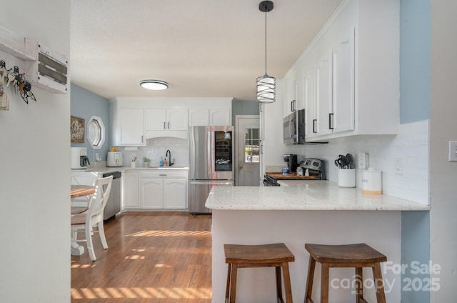 kitchen with a breakfast bar, tasteful backsplash, white cabinetry, kitchen peninsula, and stainless steel appliances