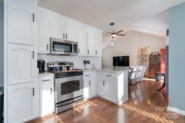 kitchen featuring white cabinetry, backsplash, kitchen peninsula, lofted ceiling, and appliances with stainless steel finishes