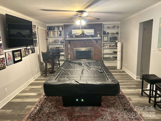 recreation room with crown molding, wood-type flooring, built in features, billiards, and a fireplace