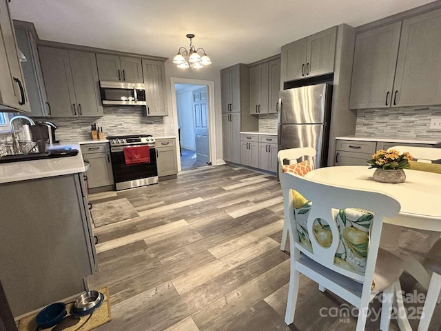 kitchen with decorative backsplash, stainless steel appliances, decorative light fixtures, an inviting chandelier, and gray cabinets