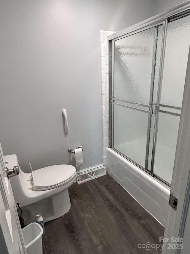 bathroom featuring hardwood / wood-style floors, bath / shower combo with glass door, and toilet