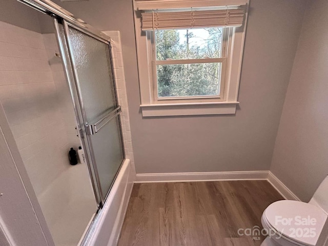 bathroom with enclosed tub / shower combo, toilet, and wood-type flooring