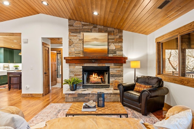 living room with vaulted ceiling, a stone fireplace, and light hardwood / wood-style flooring