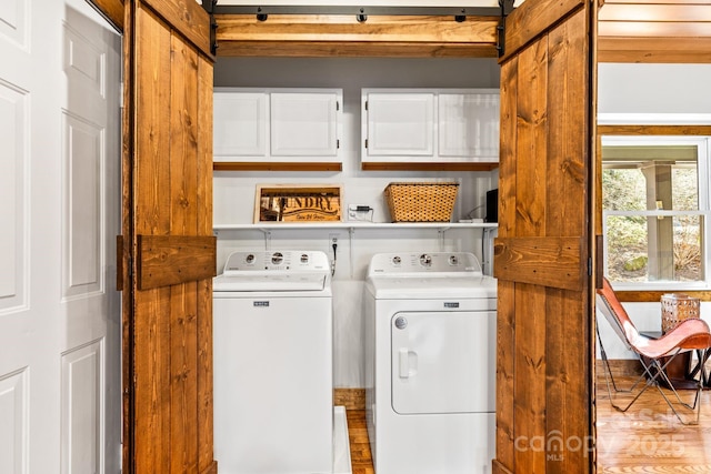 laundry area with a barn door, cabinets, light hardwood / wood-style flooring, and washing machine and clothes dryer