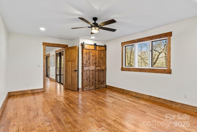 empty room featuring a barn door, ceiling fan, and hardwood / wood-style flooring