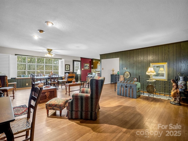 living room with hardwood / wood-style flooring, ceiling fan, a textured ceiling, and wood walls