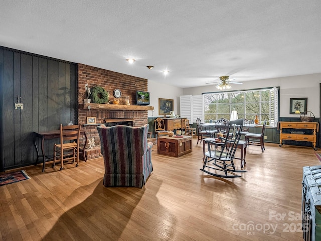 living room featuring ceiling fan, light wood-type flooring, a textured ceiling, and a fireplace