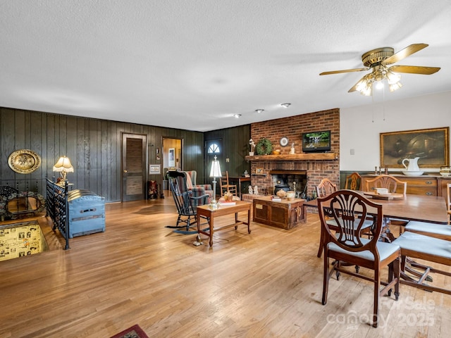 dining area with ceiling fan, a textured ceiling, a fireplace, and light hardwood / wood-style flooring