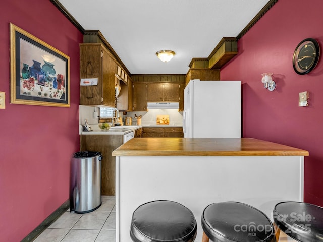 kitchen with sink, ornamental molding, light tile patterned flooring, kitchen peninsula, and white fridge