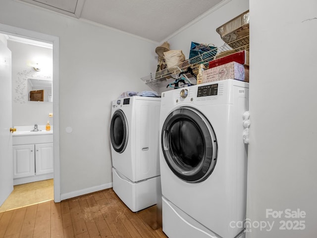 laundry area with wood-type flooring, ornamental molding, sink, and washer and clothes dryer