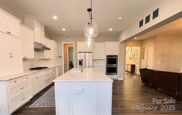 kitchen with backsplash, a center island with sink, white cabinets, hanging light fixtures, and appliances with stainless steel finishes