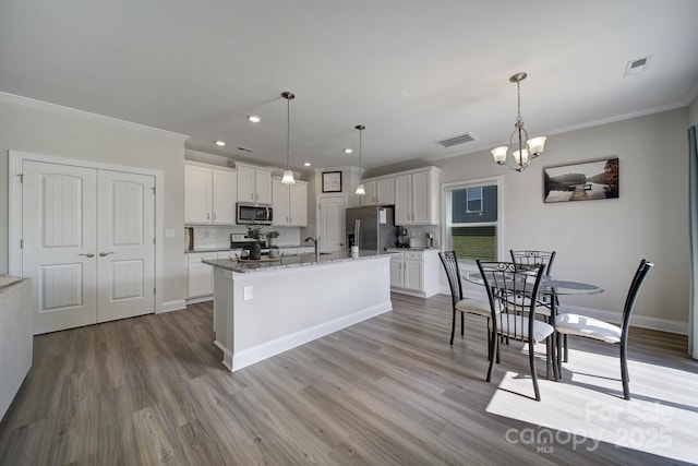 kitchen featuring backsplash, a kitchen island with sink, white cabinets, appliances with stainless steel finishes, and decorative light fixtures