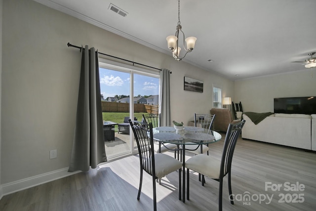 dining space with wood-type flooring, ceiling fan with notable chandelier, and ornamental molding