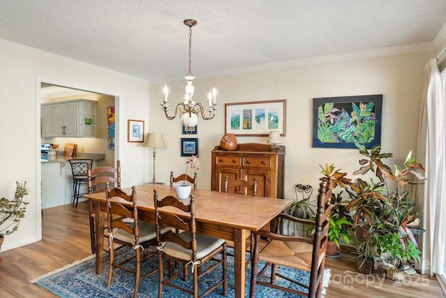 dining space with wood-type flooring, ornamental molding, a chandelier, and a textured ceiling