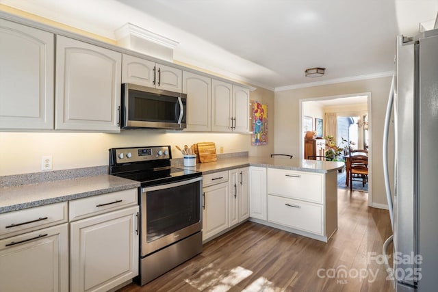 kitchen featuring dark wood-type flooring, appliances with stainless steel finishes, white cabinetry, ornamental molding, and kitchen peninsula