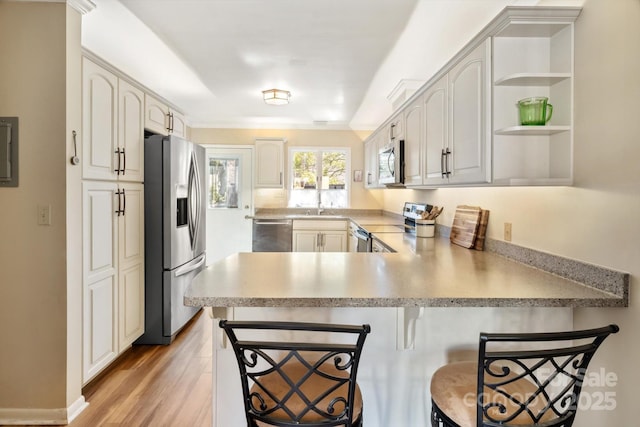 kitchen featuring a breakfast bar area, white cabinetry, kitchen peninsula, stainless steel appliances, and light hardwood / wood-style floors