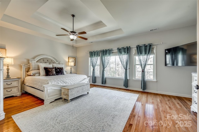 bedroom with ceiling fan, a raised ceiling, and light wood-type flooring