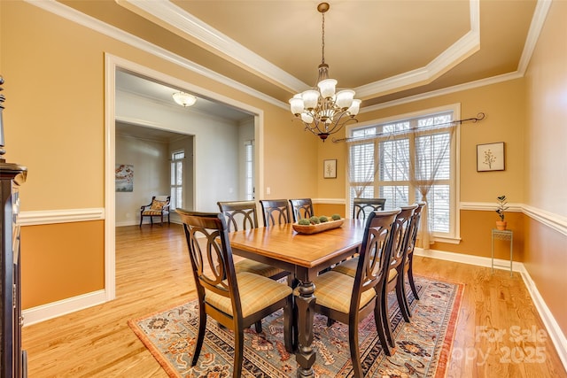 dining room featuring a raised ceiling, a notable chandelier, light wood-type flooring, and ornamental molding