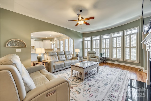 living room with light wood-type flooring, ceiling fan with notable chandelier, a fireplace, and ornamental molding