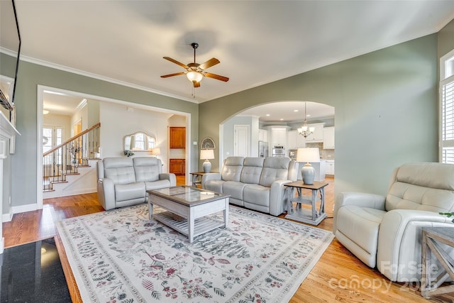 living room featuring ceiling fan with notable chandelier, light wood-type flooring, and crown molding