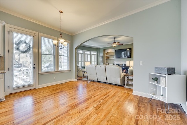 interior space with built in features, ornamental molding, ceiling fan with notable chandelier, and light wood-type flooring