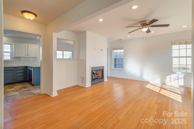 unfurnished living room featuring beverage cooler, ceiling fan, and light wood-type flooring