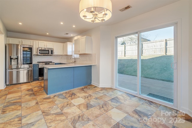 kitchen with tasteful backsplash, decorative light fixtures, appliances with stainless steel finishes, kitchen peninsula, and white cabinets