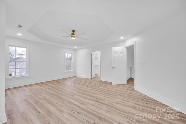 unfurnished room with ceiling fan, light wood-type flooring, and a tray ceiling