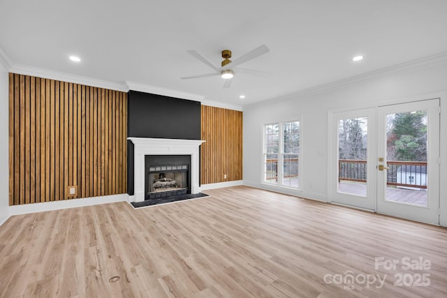 unfurnished living room with a large fireplace, ceiling fan, crown molding, light wood-type flooring, and french doors