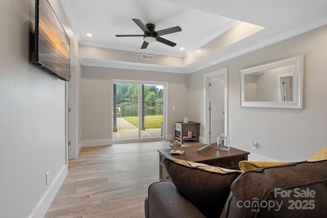 living room featuring ceiling fan, light hardwood / wood-style floors, ornamental molding, and a tray ceiling