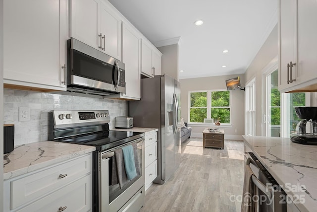 kitchen with white cabinetry, crown molding, light stone counters, and appliances with stainless steel finishes