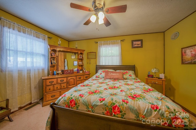 bedroom with multiple windows, a textured ceiling, light colored carpet, and ceiling fan