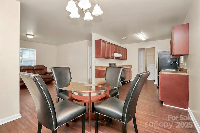 dining area featuring an inviting chandelier, dark hardwood / wood-style floors, washer / dryer, and sink