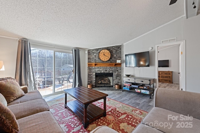 living room featuring a stone fireplace, vaulted ceiling, wood-type flooring, crown molding, and a textured ceiling