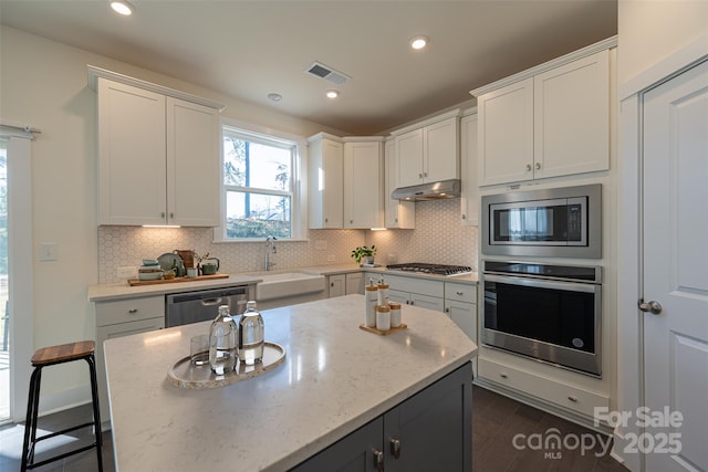 kitchen with light stone countertops, white cabinetry, sink, a center island, and stainless steel appliances