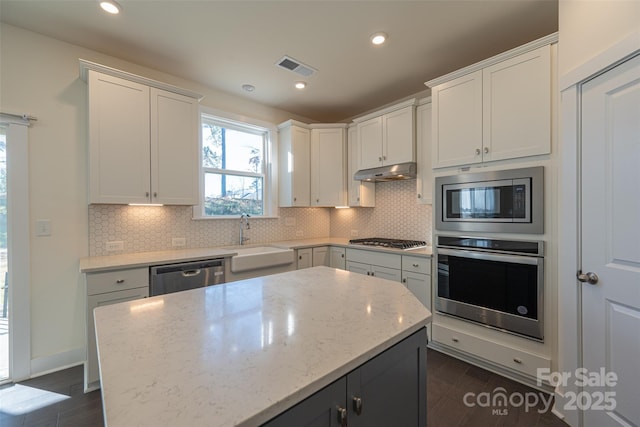 kitchen featuring light stone countertops, sink, stainless steel appliances, a kitchen island, and white cabinets