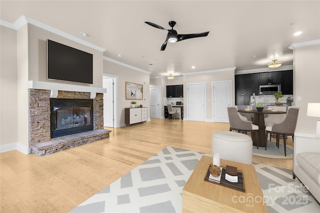 living room featuring hardwood / wood-style floors, a stone fireplace, ceiling fan, and ornamental molding