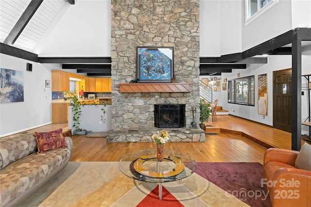 living room with a fireplace, a high ceiling, light hardwood / wood-style flooring, and beam ceiling