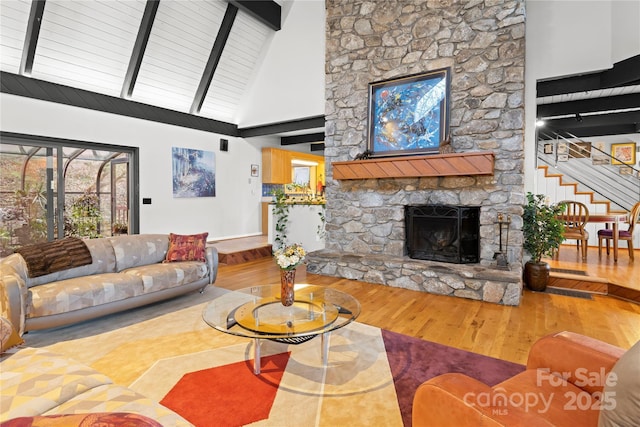 living room with hardwood / wood-style flooring, beam ceiling, a stone fireplace, and high vaulted ceiling