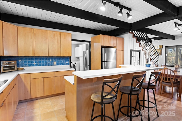 kitchen with washer and clothes dryer, a center island, decorative backsplash, stainless steel fridge, and beamed ceiling