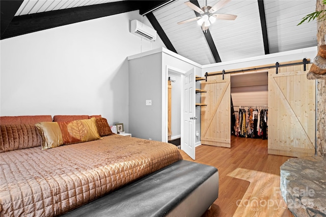 bedroom with ceiling fan, a barn door, vaulted ceiling with beams, a wall mounted AC, and light wood-type flooring