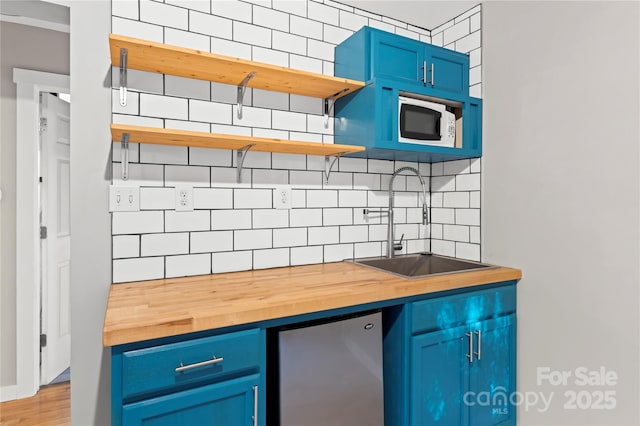 kitchen with butcher block counters, sink, blue cabinets, refrigerator, and white microwave