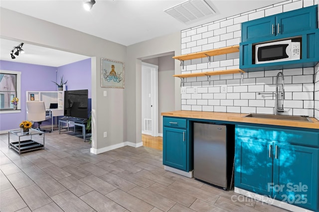 kitchen featuring white microwave, refrigerator, blue cabinets, sink, and butcher block countertops