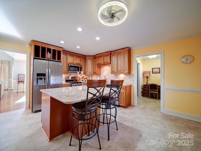 kitchen featuring appliances with stainless steel finishes, light stone counters, a kitchen island with sink, crown molding, and ceiling fan